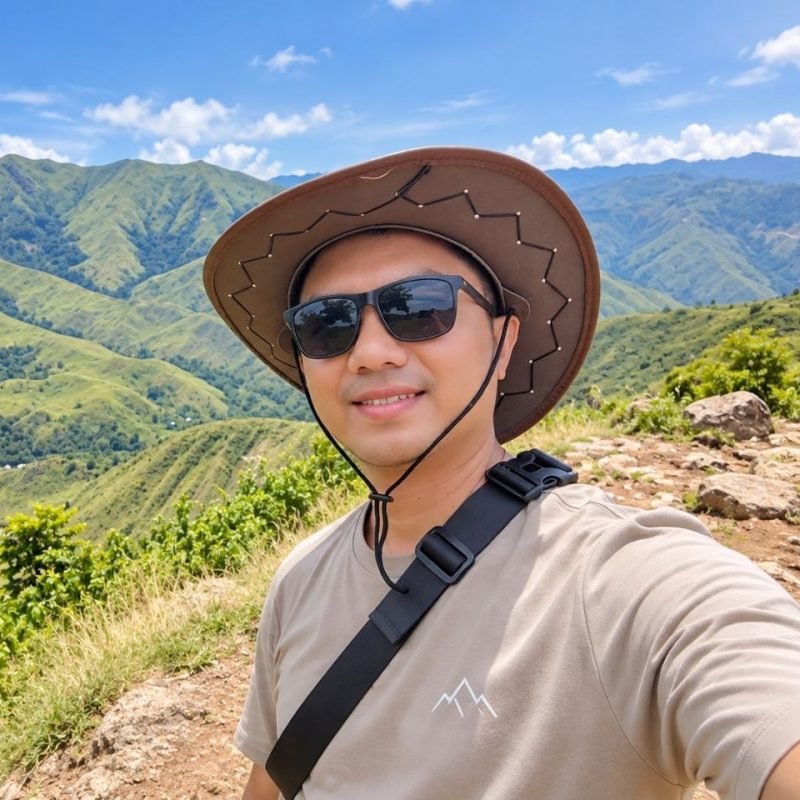 Pil, web developer, on a mountain ridge wearing a sun hat and sunglasses